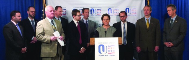Tamar Eisenstat (center), an OU Advocacy-NY lay leader, discusses the benefits of the Energy Parity Act for Jewish day schools at a press conference in Albany. She is surrounded by members of the New York State Legislature as well as by Jeff Leb (to her left, front row), director of political affairs for OU Advocacy-NY, and Maury Litwack (to her right), director of state political affairs and outreach for OU Advocacy. New York State Senator Simcha Felder is in the back row, second from left.